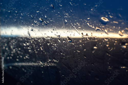 Raindrops on the side window of the car against the background of the sunset and the silhouette of a tree, a photo from inside the car