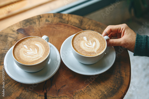 Fototapeta Dwie filiżanki aromatycznej kawy cappuccino lub latte na drewnianym stole. osoba trzyma kubek ręką. Koncepcja spotkania lub relaksu. Smaczne poranne drinki.