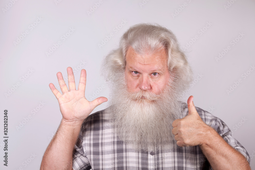 Senior thickset Caucasian happy man with splendid grey hair and beard on grey background with open hand and thumb up gesture. Attractive elderly European handsome people close up. Beautiful portrait. Senior thickset Caucasian happy man with splendid grey hair and beard on grey background with open hand and thumb up gesture. Attractive elderly European handsome people close up. Beautiful portrait.