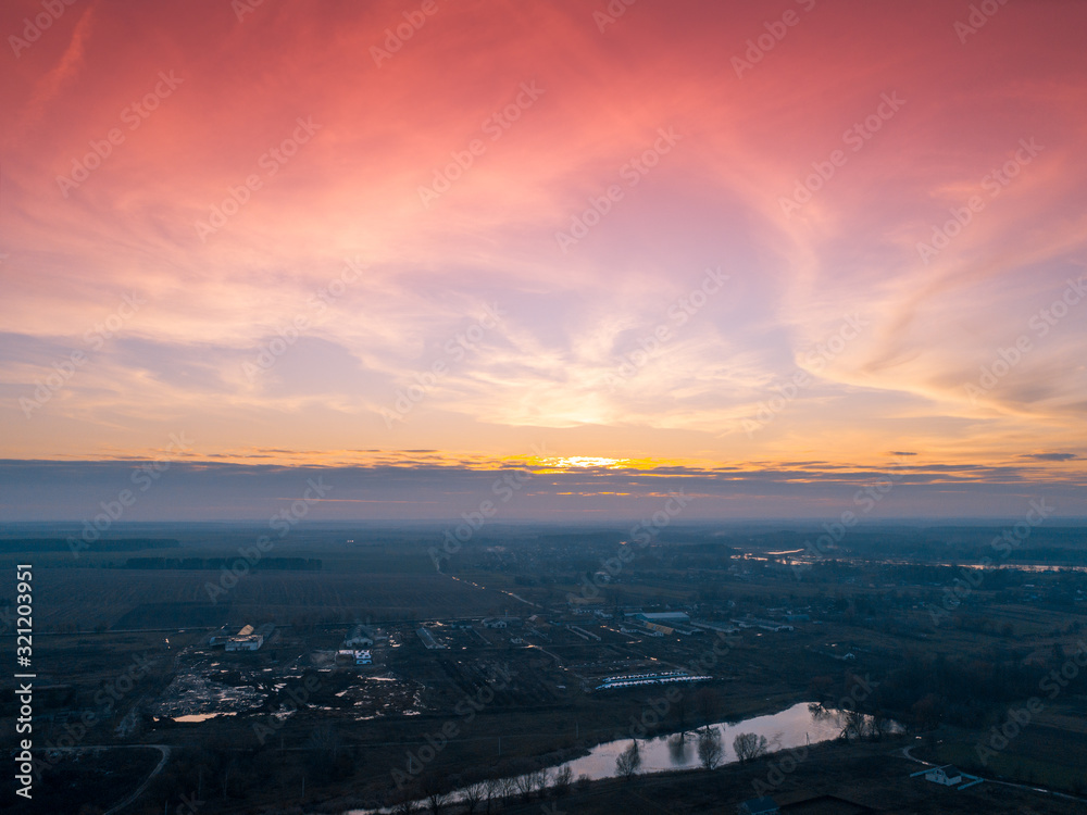 Magical sunset in the countryside in autumn. Rural landscape in the evening. Aerial view of brook, village and arable fields. Panoramic view