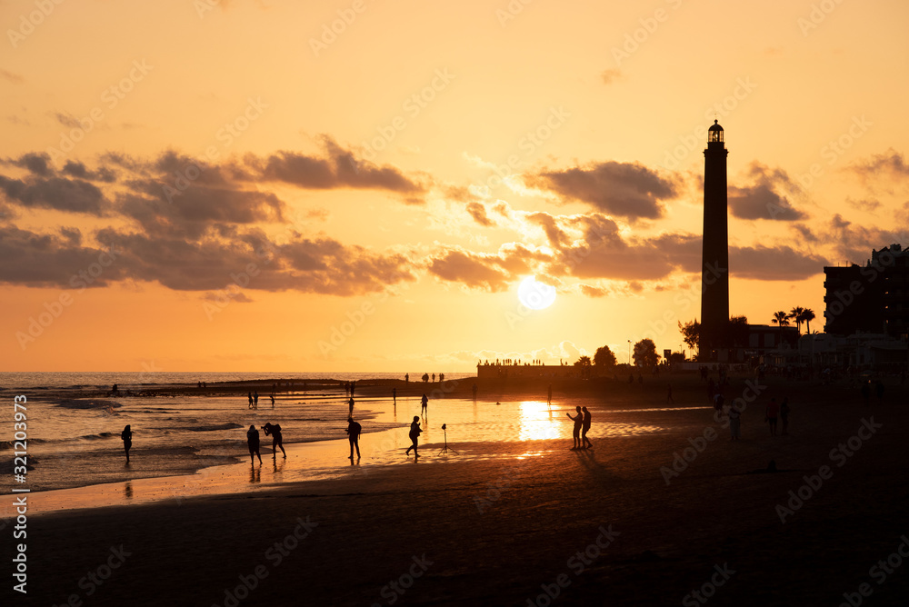 Figuras de personas a contraluz durante una puesta de sol dorada en la costa