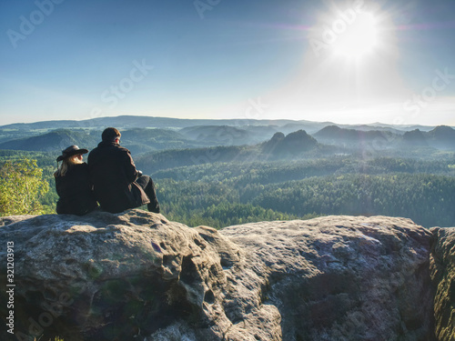 Cowgilr sit with boy friend on rocky view point above valley. Heterosexual couple have wild nature date