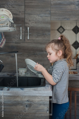 Little girl washes dishes in the kitchen photo