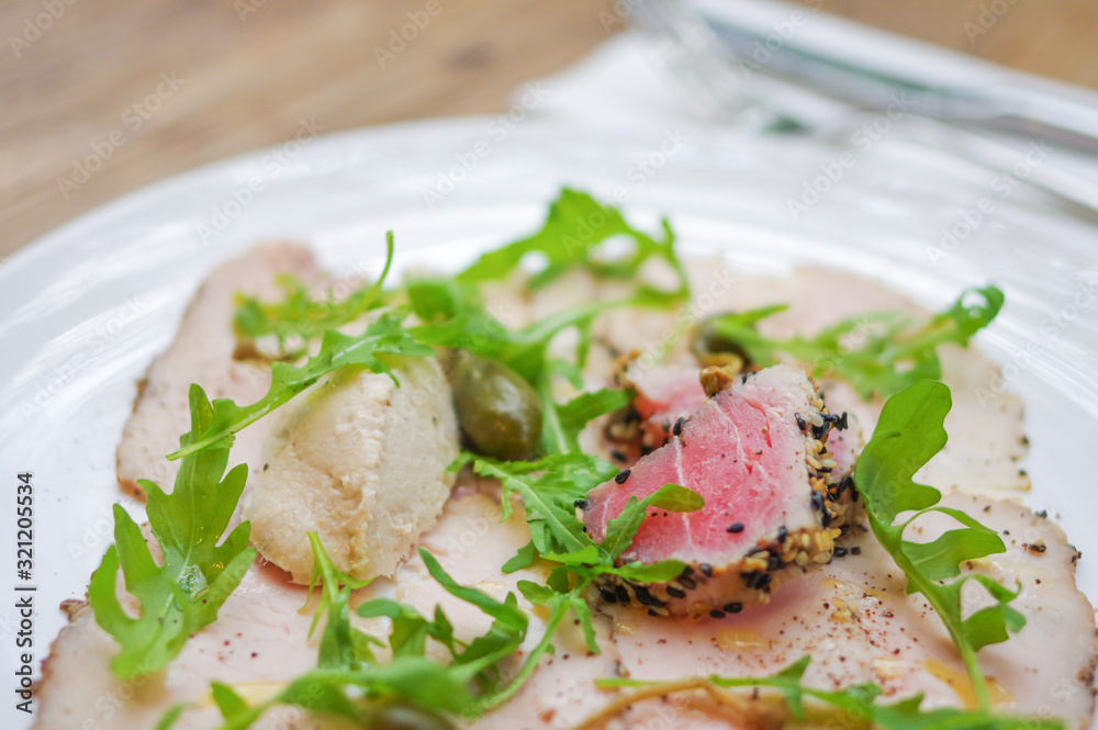Sesame crusted tuna fish meat, smoked ham and arugula leaves on white plate Sesame crusted tuna fish meat, smoked ham and arugula leaves on white plate