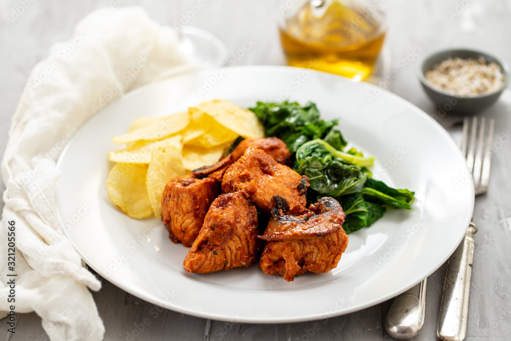 fried meat with potato chips and greens on white plate on ceramic background