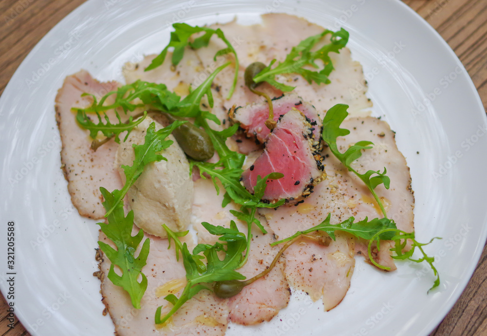 Sesame crusted tuna on smoked chicken ham and arugula salad leaves in white triangle plate top view