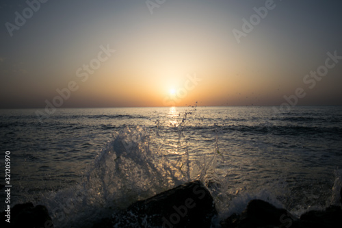 a beautiful sunrise on the seashore. the waves of the sea hit the rocks scattering water. the sun is making its appearance in a new day
