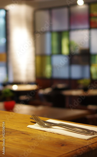 Stainless steel fork and knife with white tissue on wood table in modern empty restaurant