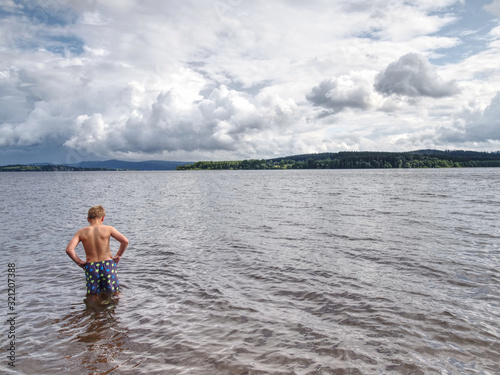 Little joyful Caucasian funny boy try cold water of lake.