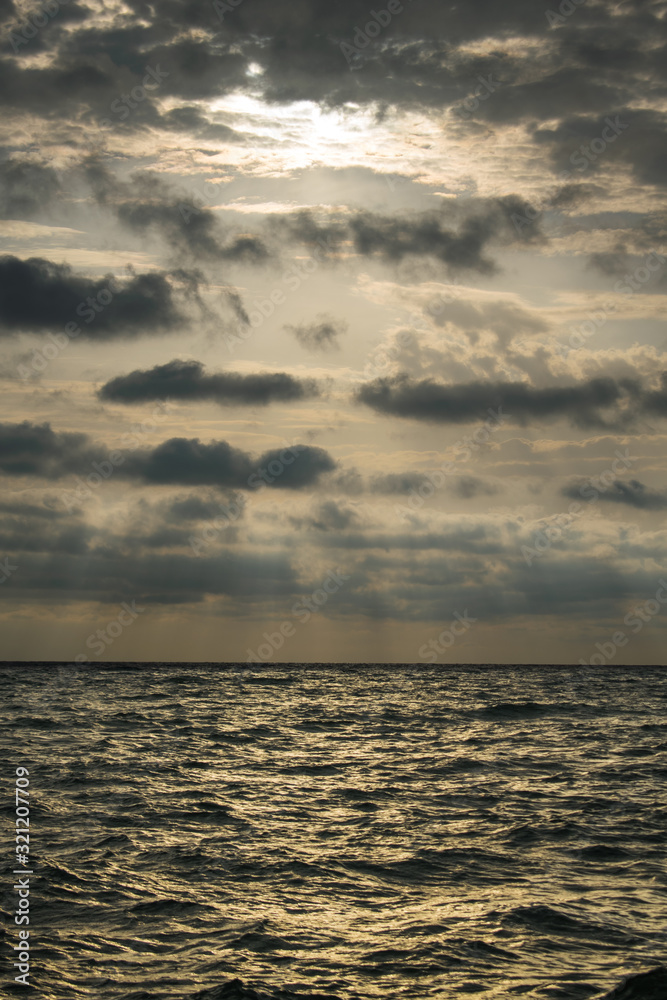 sunrise at sea, with a dramatic sky full of black clouds. A stormy summer day