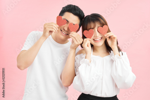 Attractive young couple holding red love hearts over eyes isolated on pink background