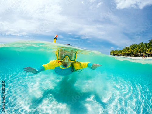 Split underwater photo of child in mask snorkeling in blue ocean water near tropical island