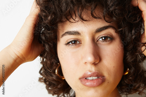 Close-up portrait of young woman with curly hair posing on the white wall. With positive emotions. Space for your text.
