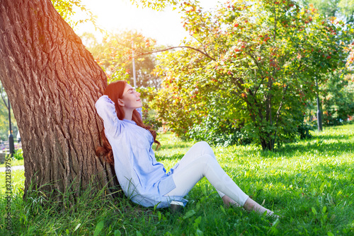 Young woman sitting under tree in summer park