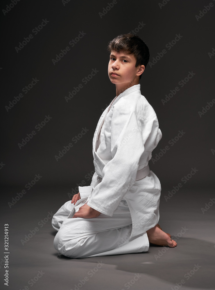 sport concept - a teenager dressed in martial arts clothing poses on a dark gray background, studio shoot
