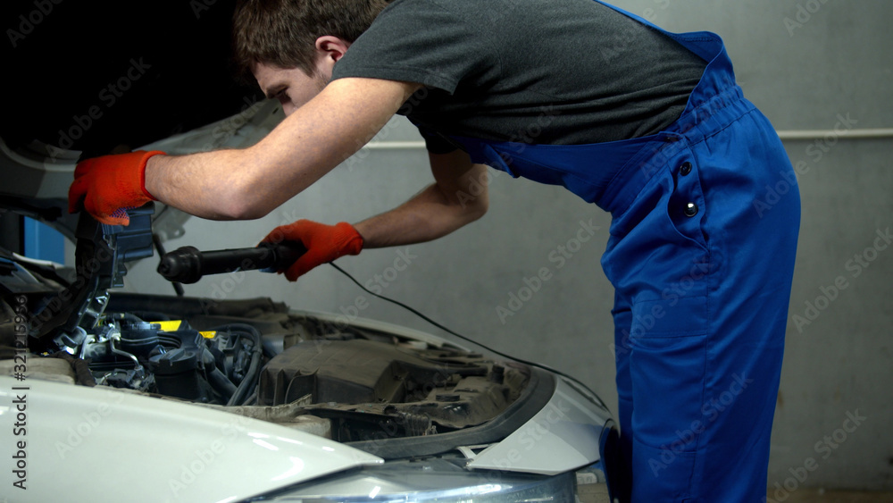 Mechanic with flashlight examines the motor of car