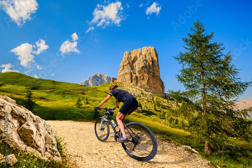 Woman cycling in Cortina d'Ampezzo, stunning Cinque Torri and Tofana in background. Woman riding MTB trail. South Tyrol province of Italy, Dolomites.