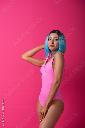 Pretty woman in a pink monokini and blue wig in the studio. Girl with artificial short hair posing in a colored swimsuit. © Михаил Решетников
