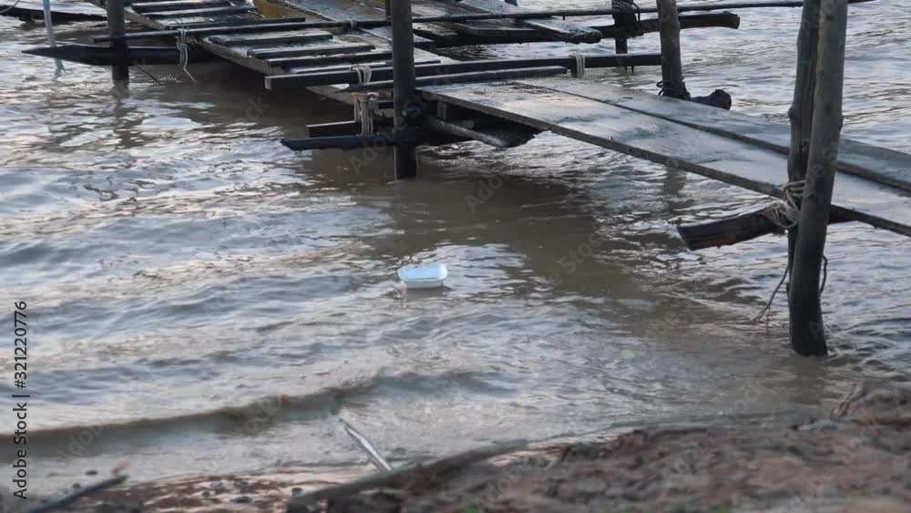 medium shit of a old wooden jetty going out to a lake with a piece of polystyrene floating along the shoreline as the waves move it