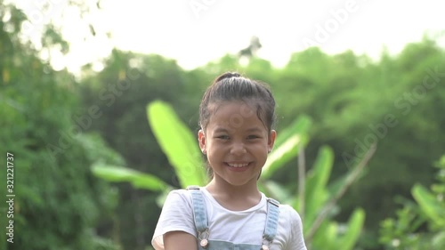 slow motion shot. A happy little girl in a white t-shirt with a long haircut is smiling at the camera on the nature outdoors.