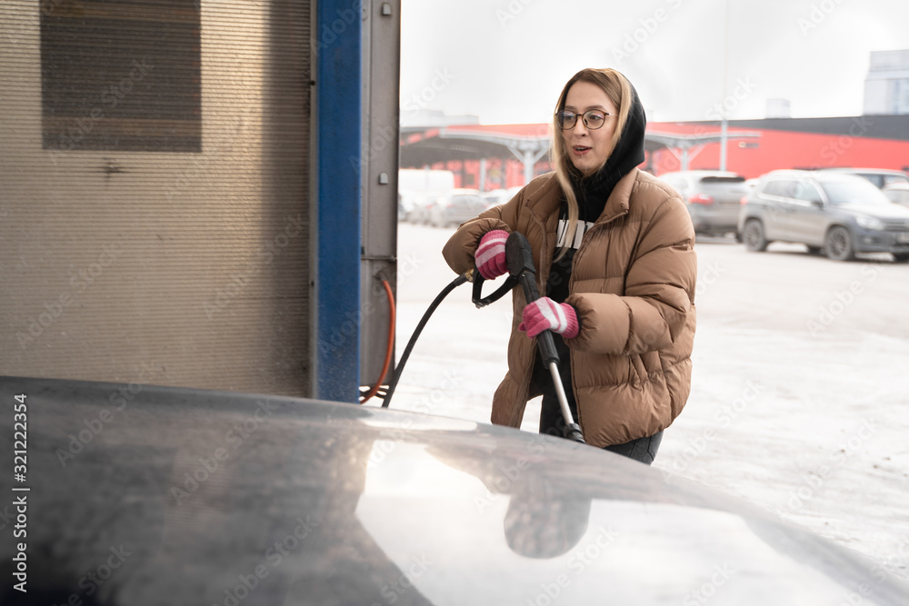 The girl in warm clothes wash dirty car outdoor in winter cold time. wet works.