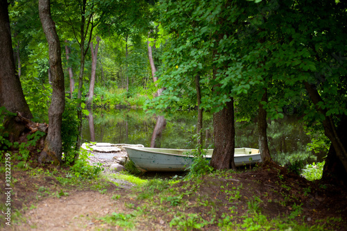 Boat on the Bank of a calm river, reflections of green trees