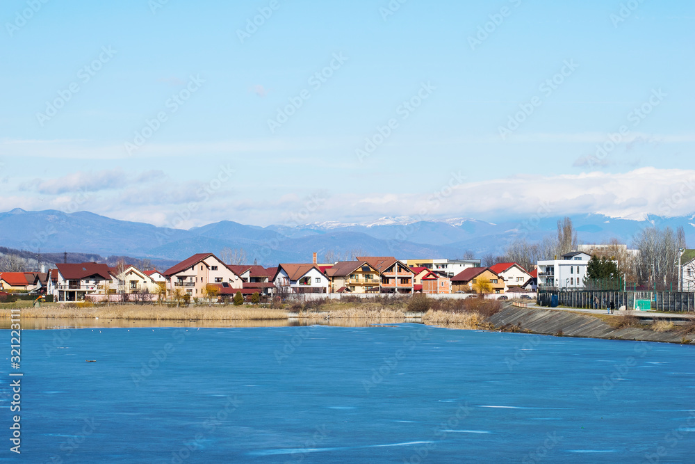 A village on the edge of a frozen lake, near the mountains.