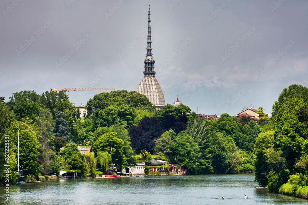 Po river in Turin, the river winds its way through lush vegetation, rowers enjoy good weather, on the ground the characteristic architecture of the Mole Antoneliana and Alps 