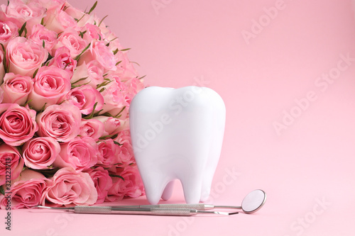 White tooth with dental instruments on a pink background with pink roses in honor of the international dentist day February 9