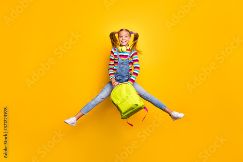 Full size photo cheerful schoolchild jump wear headset striped sweater jeans denim bag rucksack enjoy primary school lesson isolated over bright shine yellow color background