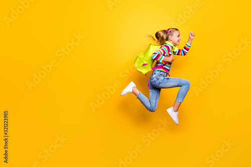 Full length photo of cheerful kid jump run speedy lesson wear striped sweater denim jeans suspenders overalls sneakers rucksack backpack isolated over bright shine yellow color background