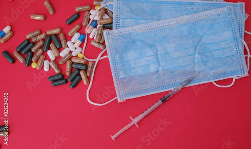 A bunch of pills, medical mask and syringe on red background