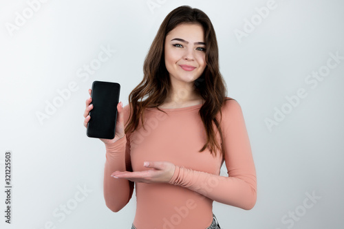 young beautiful brunette woman standing on isolated white background showing smarpthone, technology and device concept