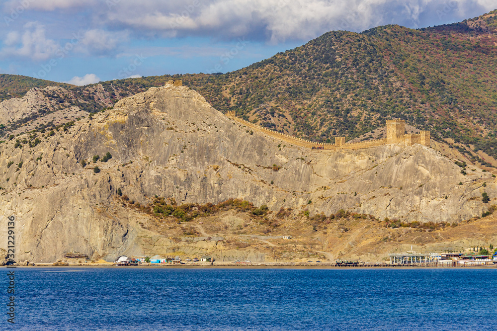 View of fortress wall of  Genoese fortress from Cape Alchak. Oldest tourist attractions of resort town is located on steep cliffs emerging from depths of sea. Sudak, Crimea, Russia, October  2019.