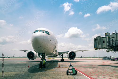 technician or engineer safety check of modern passenger or cargo airplane parking at terminal gate of international airport on a cloudy blue sky background