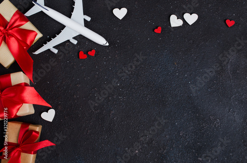 Holiday Travel Planning. Gift Travel Concept. Airplane model, gift boxes and red hearts on dark background.