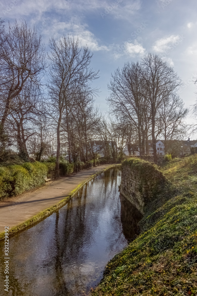 A scenic view of a water way along a path, trees and vegetal bank under a majestic blue sky and white clouds A scenic view of a water way along a path, trees and vegetal bank under a majestic blue sky and white clouds