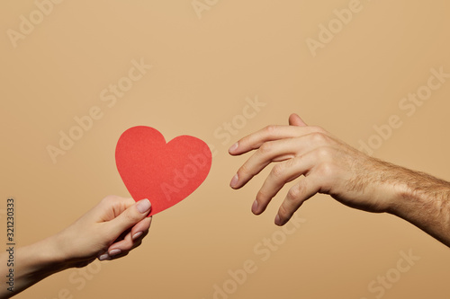 cropped view of woman holding red heart and man reaching it isolated on beige