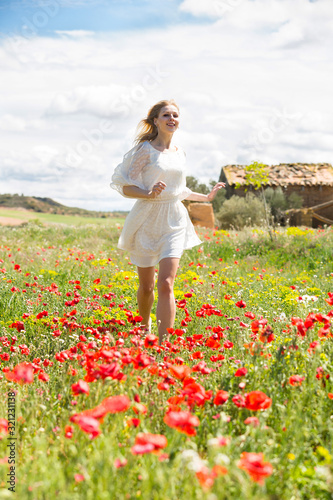 Young woman running in field with poppies plants