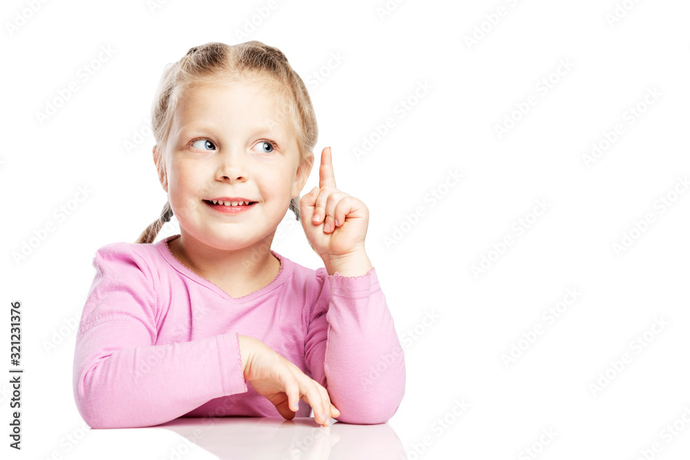 A little girl in a pink sweater is sitting at the table and raised her index finger up. Isolated on a white background. Space for text. A little girl in a pink sweater is sitting at the table and raised her index finger up. Isolated on a white background. Space for text.
