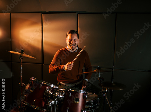 Portrait of a happy drummer playing drums and smiling at camera.