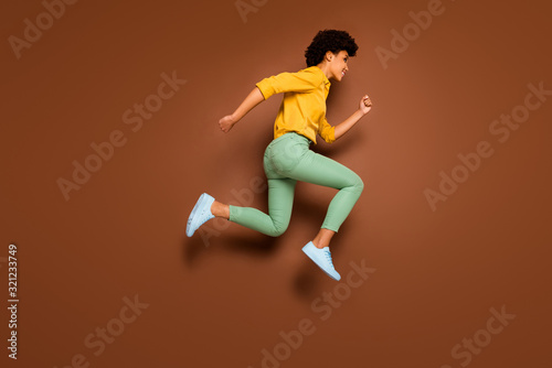 Full length photo of funny dark skin lady jumping up high rushing discount shopping center black friday wear yellow shirt green pants footwear isolated brown color background