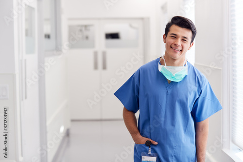 Portrait Of Young Male Doctor Wearing Scrubs Standing In Hospital Corridor photo