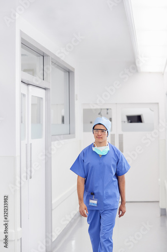 Young Male Doctor Wearing Scrubs Walking Along Hospital Corridor
