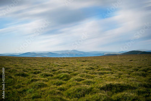 grass covered grassland  in a mountain area. The mountains can be seen somewhere in the distance