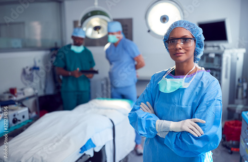 Portrait Of Female Surgeon Wearing Scrubs And Protective Glasses In Hospital Operating Theater photo