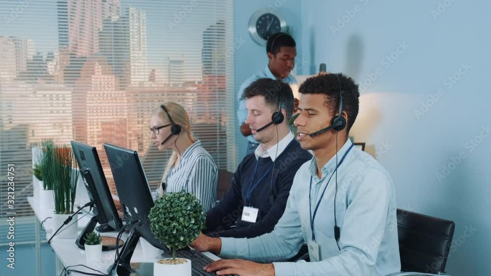 Chief black manager of the call center giving recommendations to customer service representative, which making international call to the client.