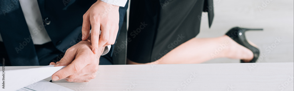 panoramic shot of secretary touching hand of businessman in office