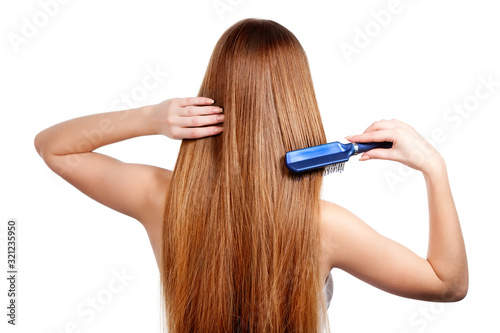 Woman combing long shiny brown hair with hairbrush, back view, isolated on white background