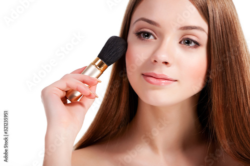 Girl with long flowing brown hair applying blush with brush, smiling and looking away, portrait on white background